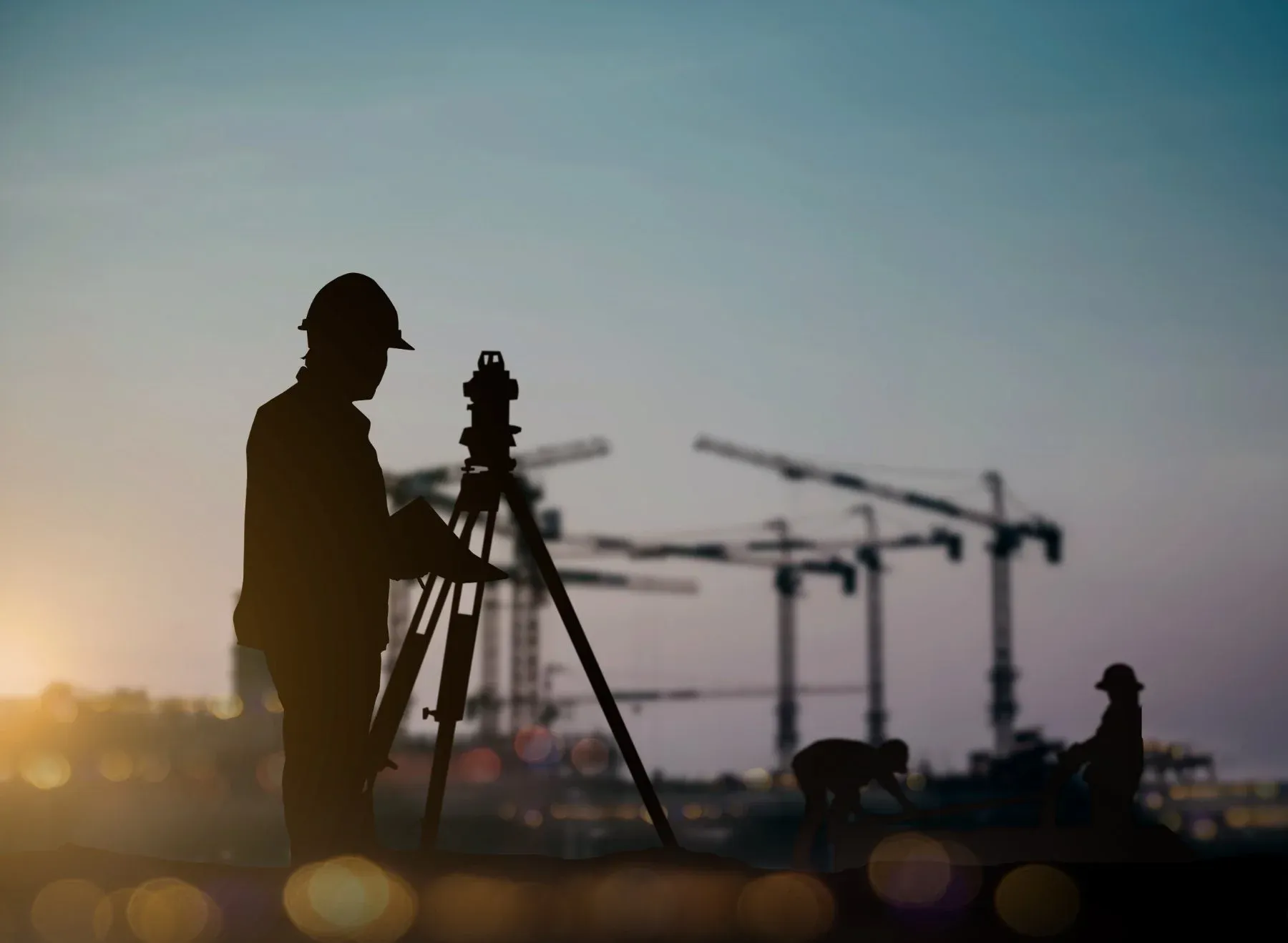 Silhouette of a surveyor using a theodolite on a construction site at sunset
