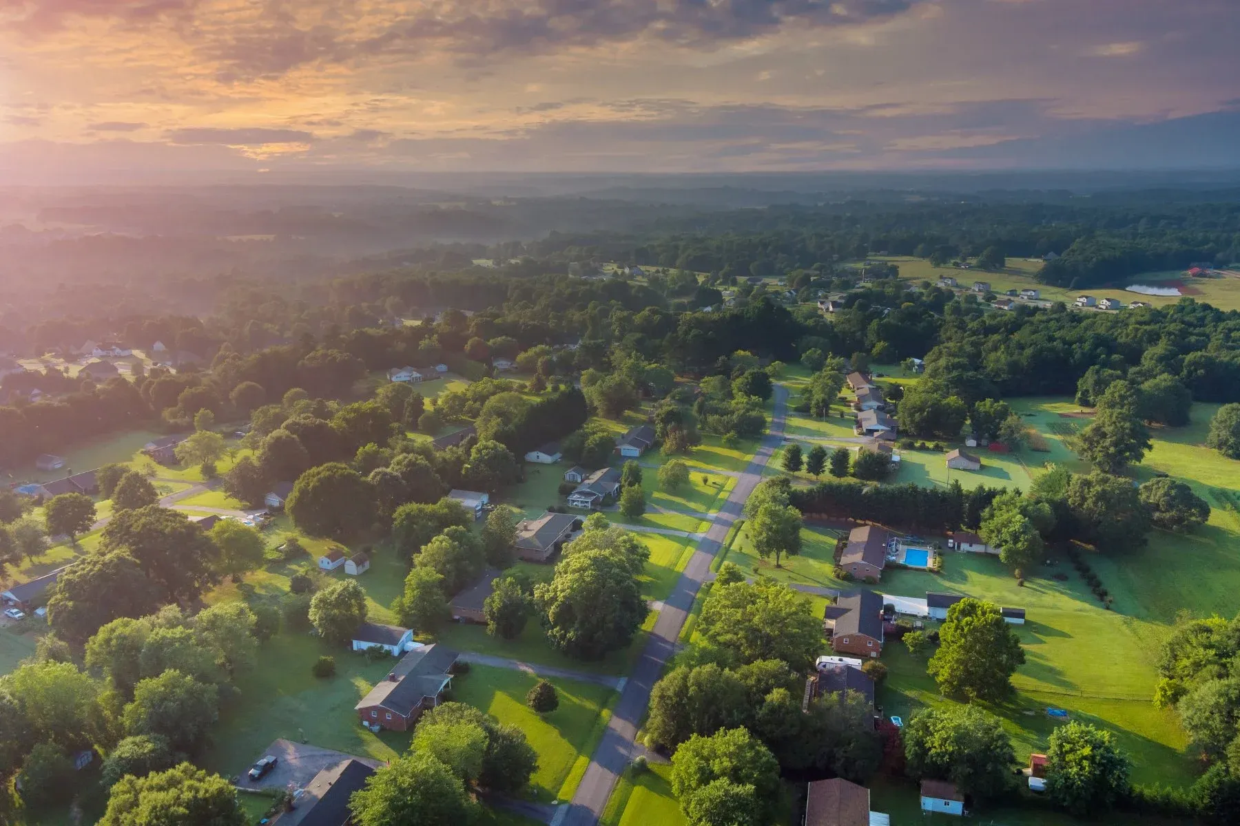 Aerial view of a rural neighbourhood with tree-lined roads at sunset