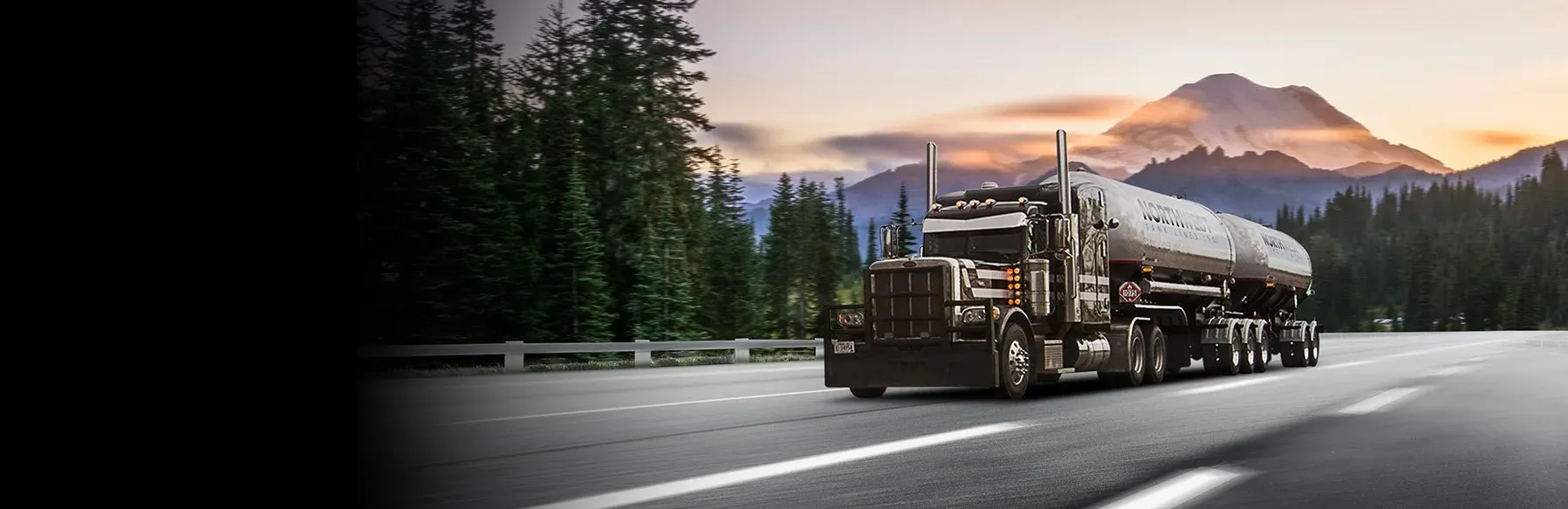 Tanker truck driving on a highway through a forested mountain valley