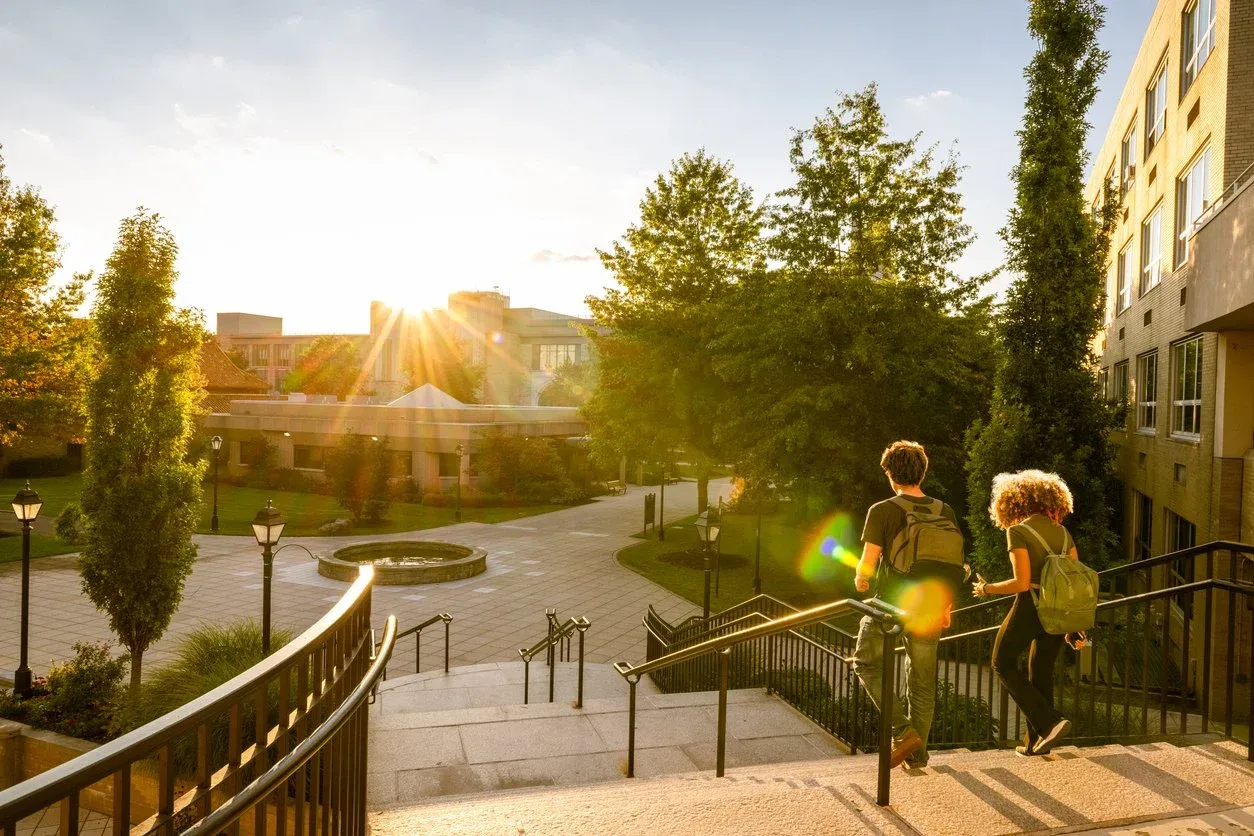 Two students with backpacks walking down campus steps in the evening sun