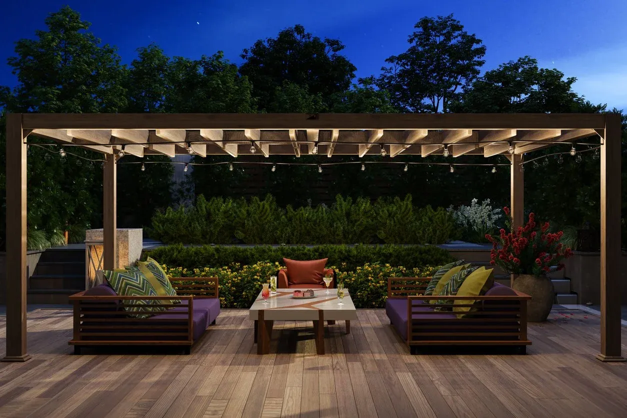 Backyard patio with a wooden pergola, outdoor sofas and string lights at night